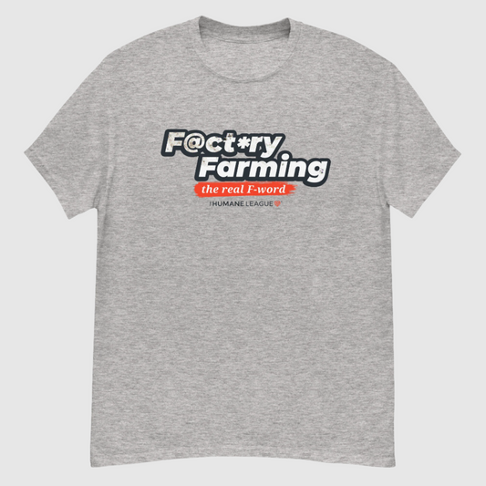 A heather gray short sleeve T-shirt with the words "F@ct*ry Farming" in large, bold letters on the front. Below, in smaller text, it says, "the real F-word" in white inside a bright red brush stroke effect. Underneath, it reads "The Humane League" in smaller font with a small red geometric heart icon next to it.