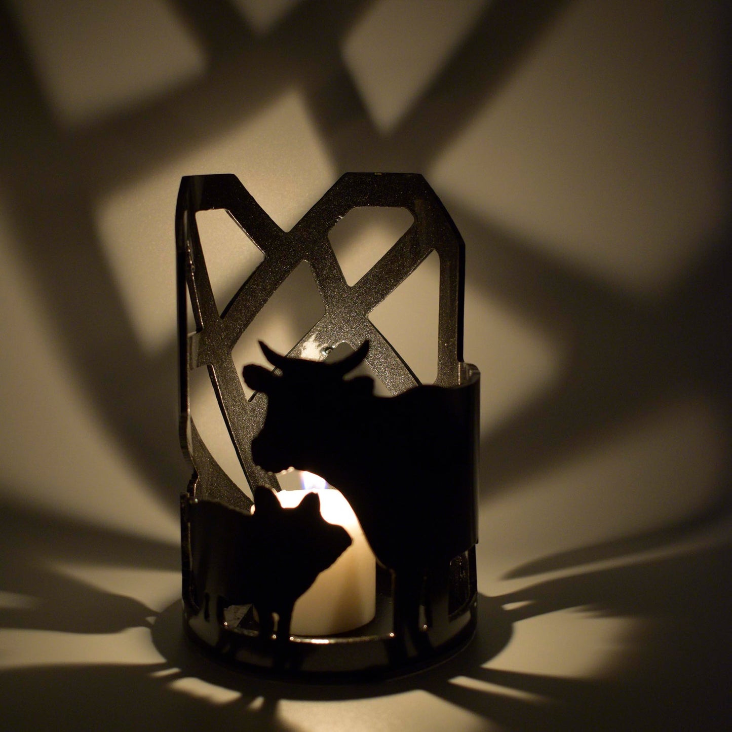Candle holder showing pig and cow silouettes lit by a small white candle to cast shadows of the animals and the Mended Heart on the walls.