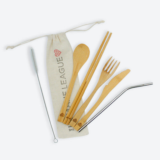 A set of eco-friendly utensils made from bamboo and a stainless steel straw, displayed alongside a beige cotton drawstring pouch with The Humane League logo printed on it. The set includes a bamboo fork, knife, spoon, chopsticks, a metal straw, and a cleaning brush for the straw.