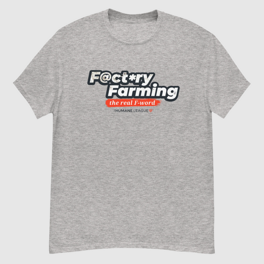 A heather gray short sleeve T-shirt with the words "F@ct*ry Farming" in large, bold letters on the front. Below, in smaller text, it says, "the real F-word" in white inside a bright red brush stroke effect. Underneath, it reads "The Humane League" in smaller font with a small red geometric heart icon next to it. 