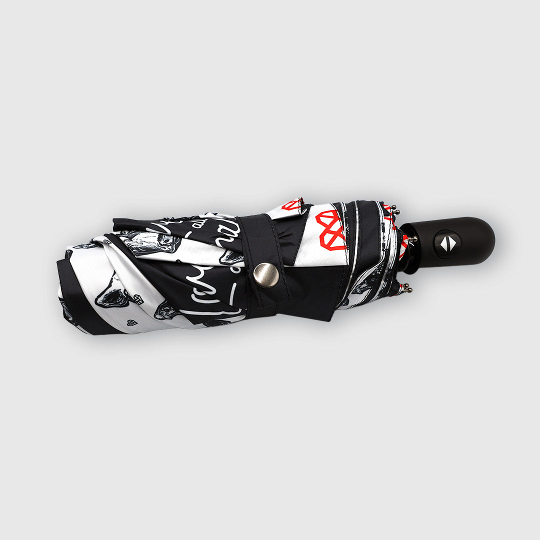 A folded compact black and white patterned umbrella with red accents, featuring a black handle and a silver snap button, shown on a light gray background.