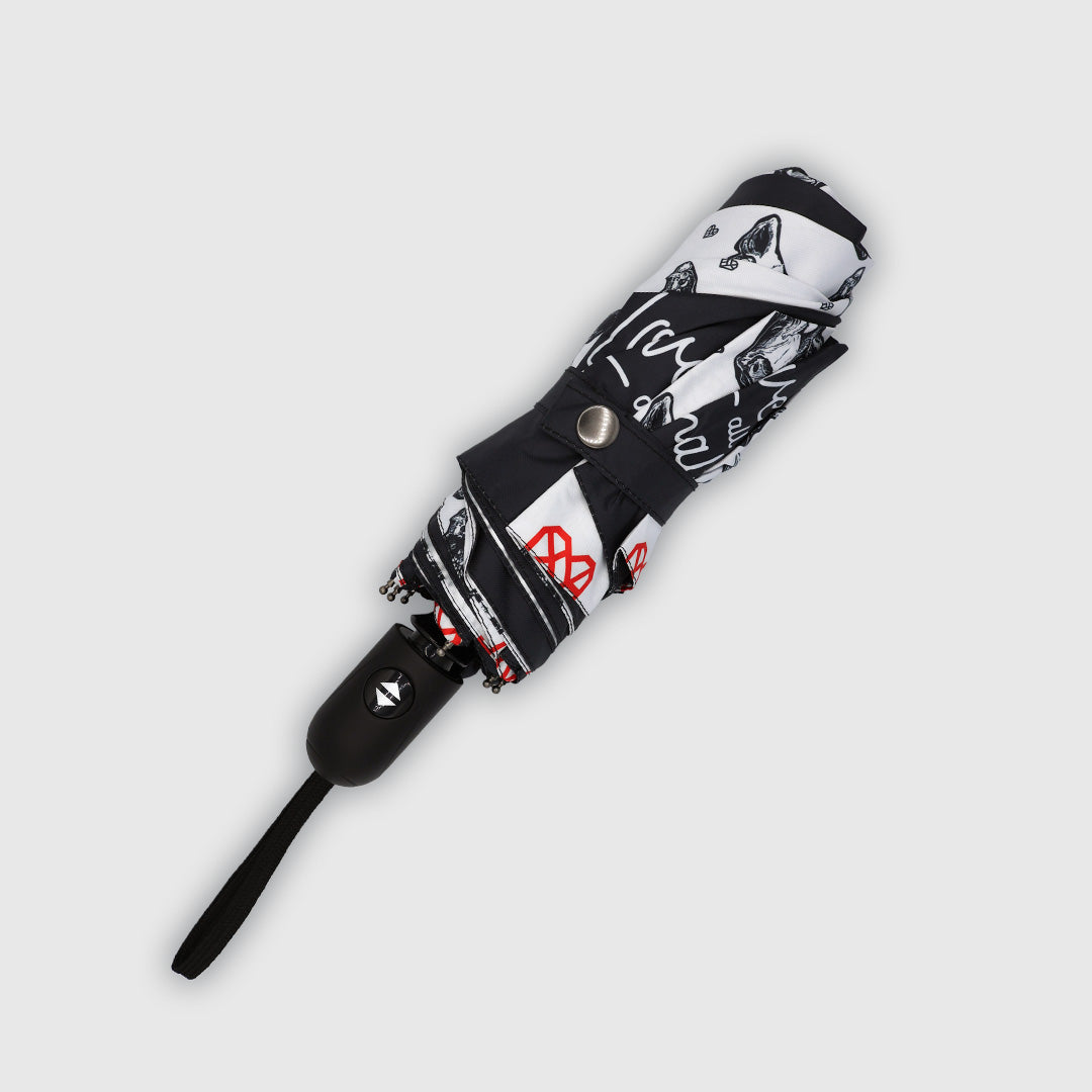 A folded compact black and white patterned umbrella with red accents, featuring a black handle and a silver snap button, shown diagonally on a light gray background.