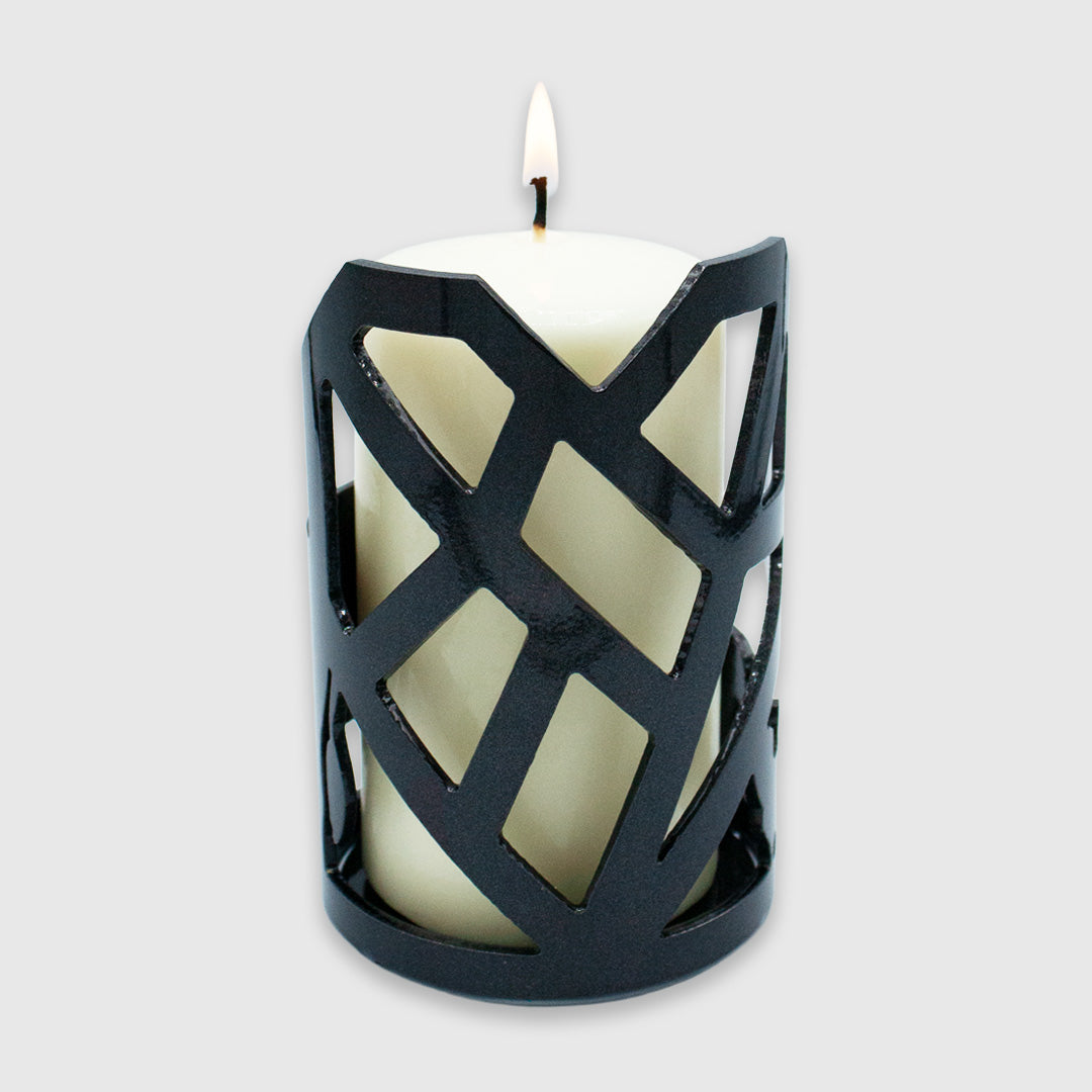 A large white candle that is lit in the candle holder showing the side with the Mended Heart cut out.