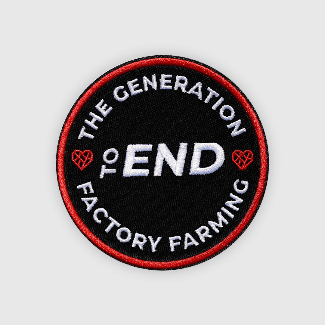 A circular embroidered patch with a black background, red border, and white text reading “THE GENERATION TO END FACTORY FARMING,” with small red heart-like farm icons on the sides, shown on a light gray background.