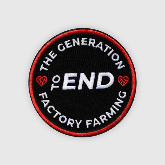 A circular embroidered patch with a black background, red border, and white text reading “THE GENERATION TO END FACTORY FARMING,” with small red heart-like farm icons on the sides, shown on a light gray background.