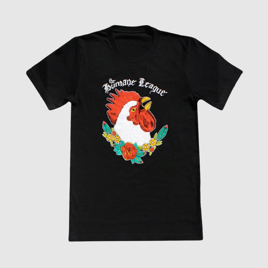 Black short sleeve t-shirt with large chicken design on the front. The Humane League is written in a hand-drawn script above the chicken. The chicken is shown from the neck up and is boldly looking upward. Red roses, yellow flowers, and green leaves weave together underneath the chicken image.