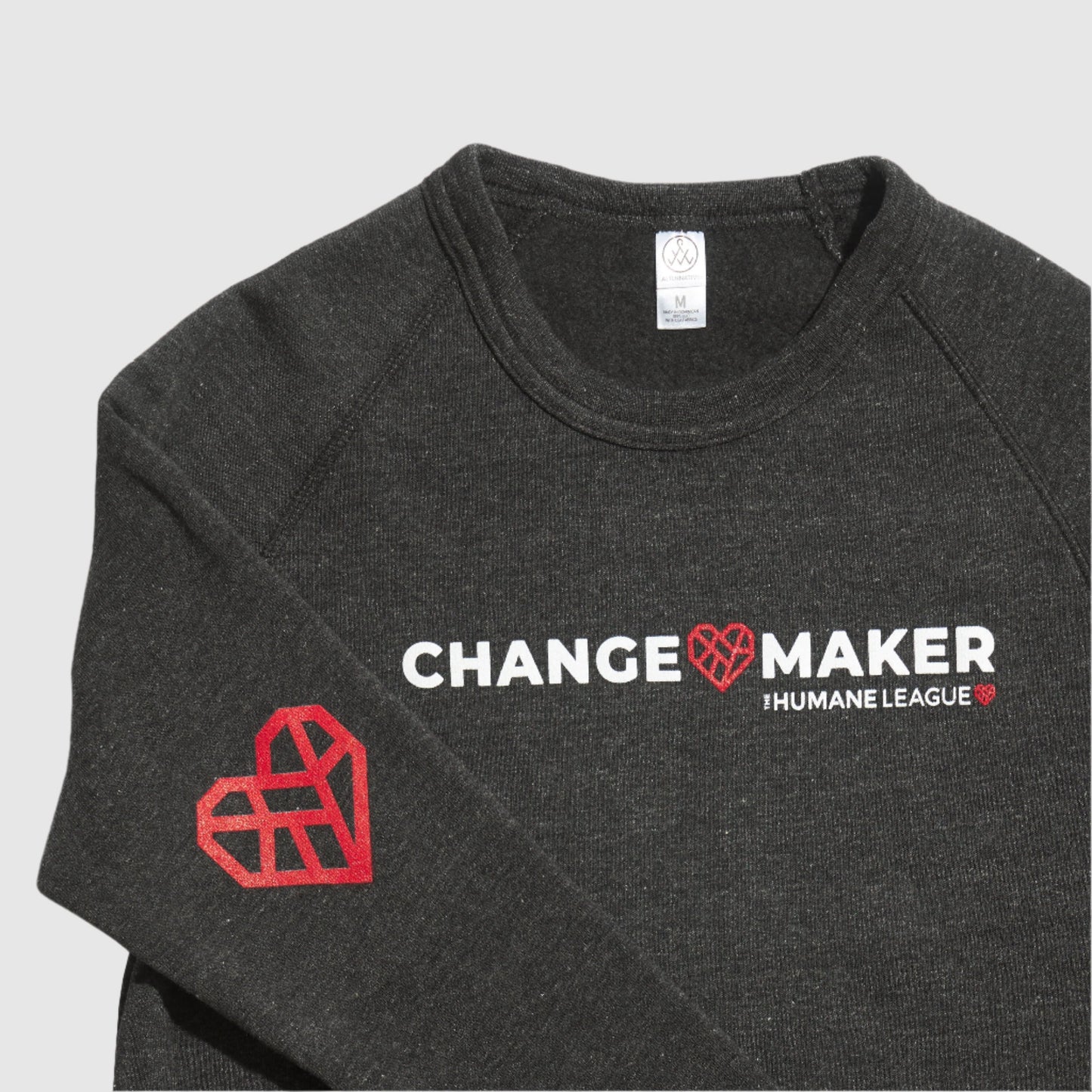 Close up of the sweatshirt showing the front Changemaker design. The sleeve is folded over to show The Humane League's red Mended Heart icon is printed on the elbow.