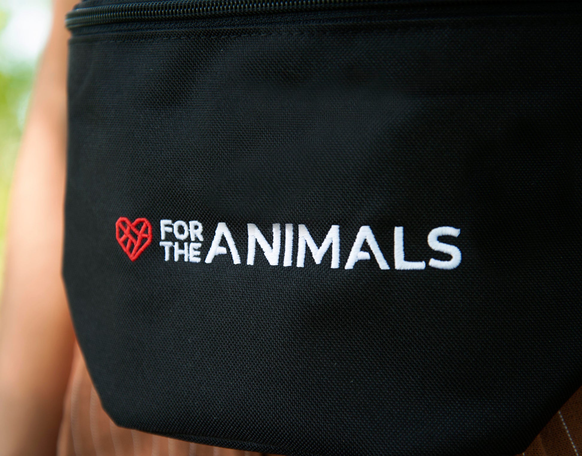 Close up of black fanny pack. The fanny pack features the slogan "For the Animals" in white text with a small red geometric heart icon.