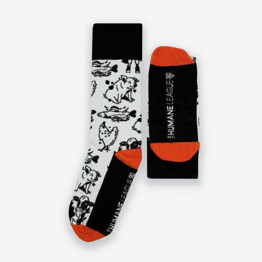 A pair of socks featuring black and white illustrations of cows, pigs, fish, and chickens. The toe and heel are bright red. The top and bottom are solid black. The Humane League logo is on the bottom of the socks.