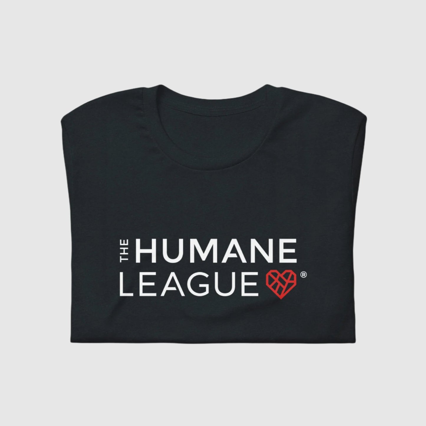 A folded dark gray t-shirt with "THE HUMANE LEAGUE" printed in white, using an all-caps font across the chest. Next to the text is a red geometric heart icon. 