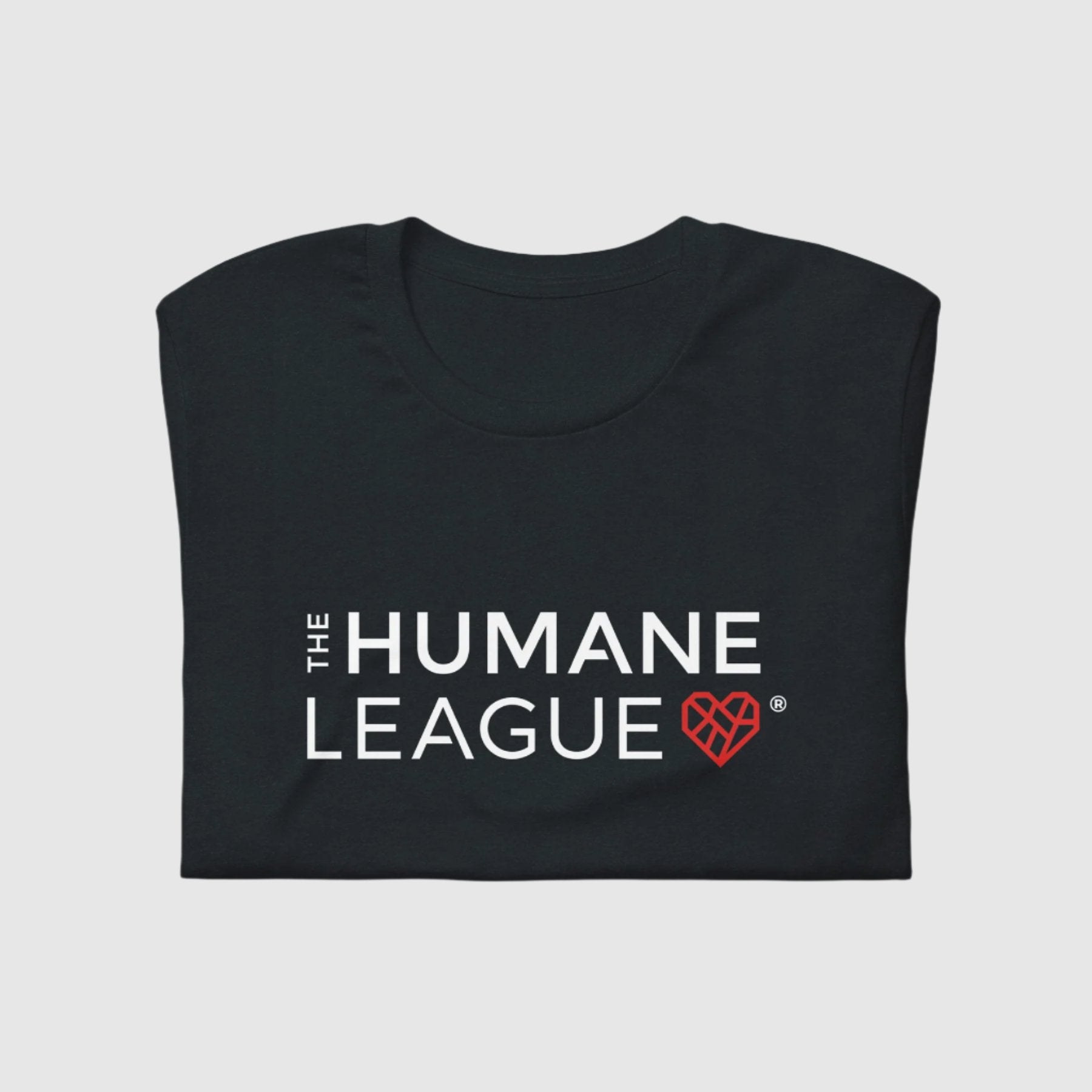 A folded dark gray t-shirt with "THE HUMANE LEAGUE" printed in white, using an all-caps font across the chest. Next to the text is a red geometric heart icon. 