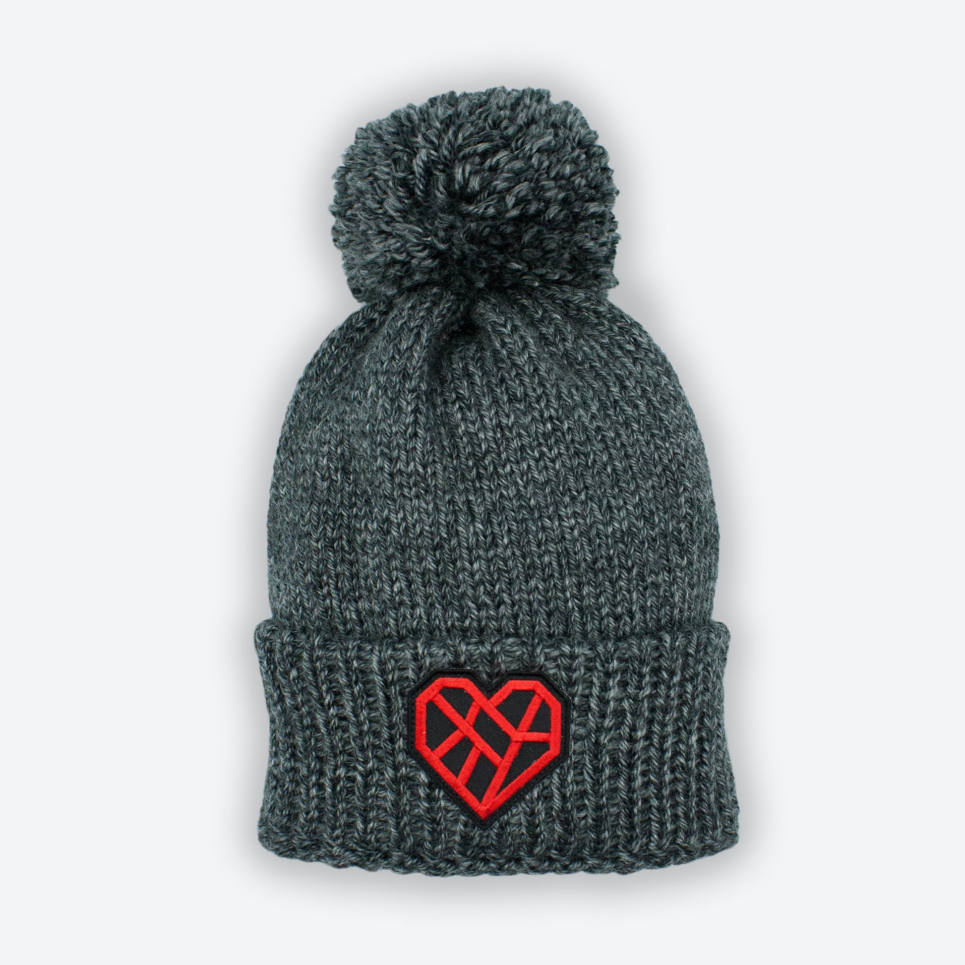 Chunky charcoal gray color knitted beanie hat. It has a wide cuff on the bottom and a large pom pom on top. An embroidered Mended Heart patch in on the front cuff on the beanie. The Mended Heart has angular lines that are a warm and bright red in color. They form a heart shape on a black background.